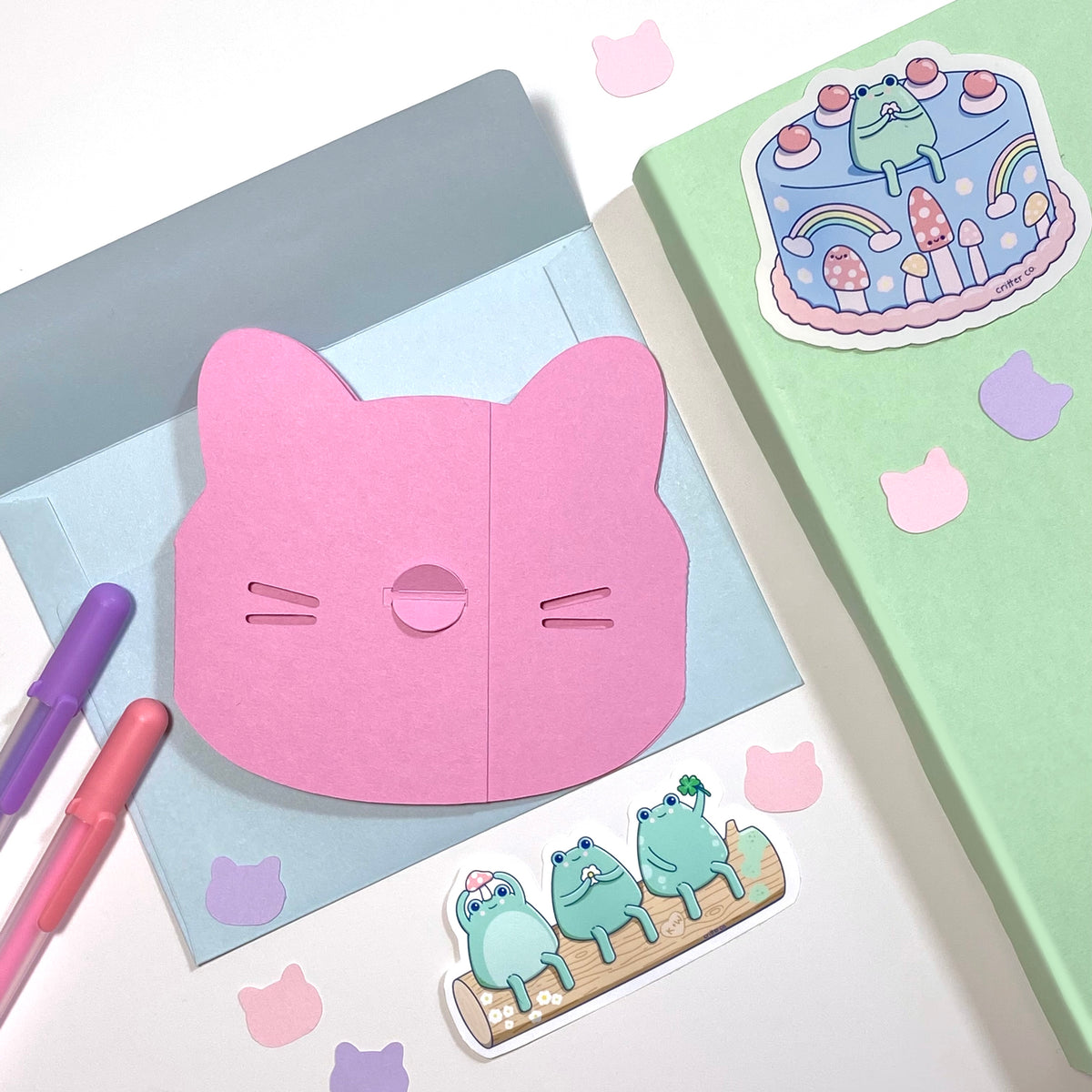 Kawaii stickers on journal with a die cut cat card. The custom digital art stickers are bright pastel colors surrounded by office supplies and cute confetti. Critter Co. brand name is on the stickers.